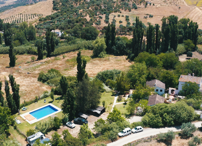 Birds-eye view of Finca Vegana with the pool, parking lot, holiday homes, riverbed and grassland